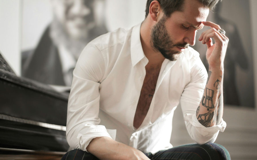 Man with tattoos, seated at a piano, thiking intently